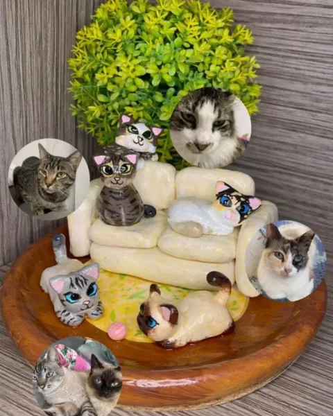 Miniature clay sculpture of five cats on and around a cream sofa on a wooden base, shown next to photos of the real cats it was modelled on.